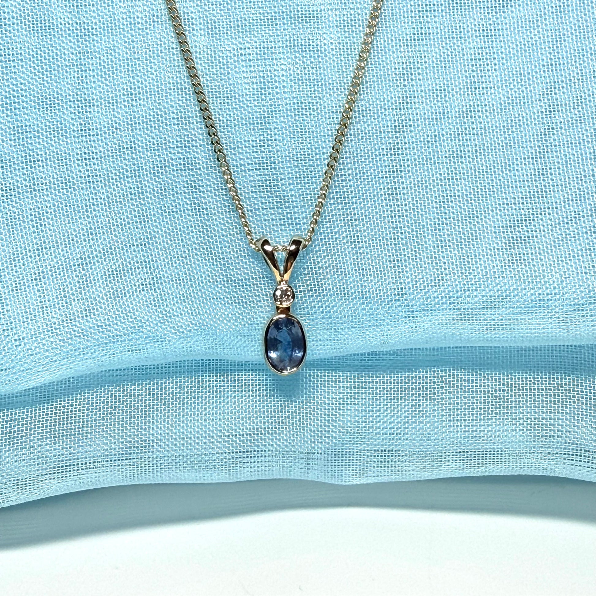 Gold necklace with a blue pendant on a light blue fabric background