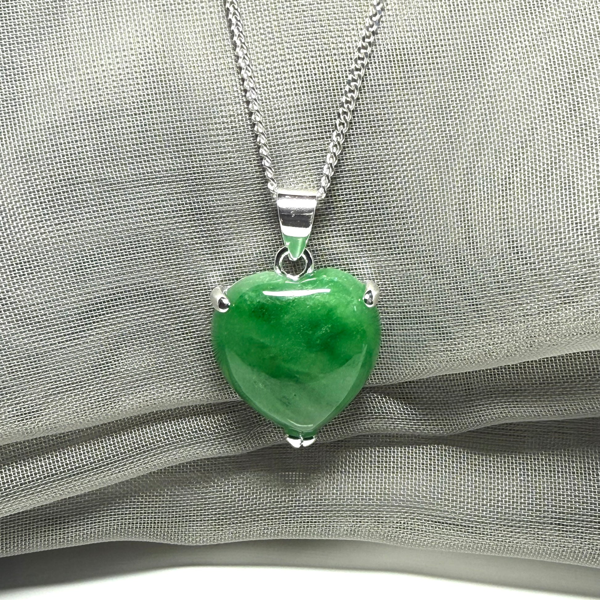 Green heart-shaped pendant on a silver chain against a gray fabric background