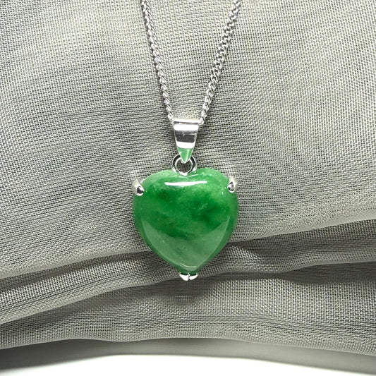 Green heart-shaped pendant on a silver chain against a gray fabric background